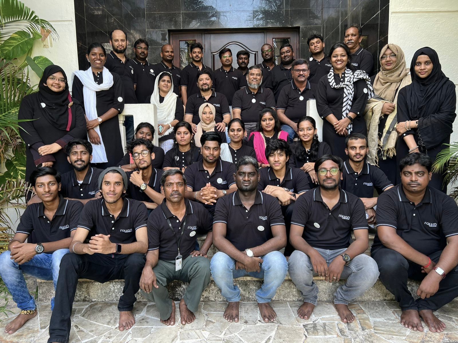The Rayan Architects studio seated together on the entrance steps in black studio shirts